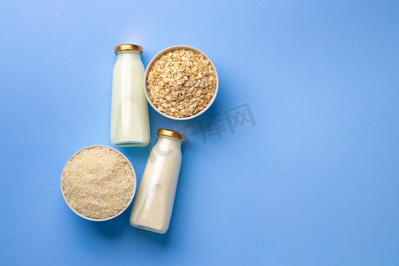大米和牛奶摄影照片_蓝色背景中玻璃瓶中的燕麦和大米素食牛奶