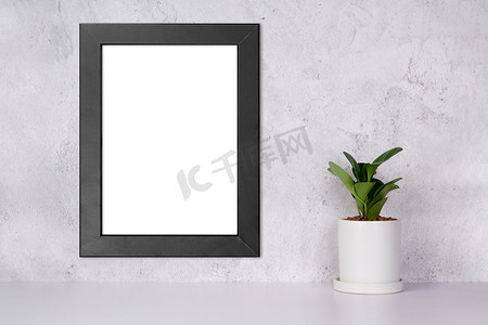 照片展示模板摄影照片_墙上垂直的模型黑色框架和家里桌面上盆栽的植物，桌面上展示的模型海报，画廊照片和图片的设计，广告边框模板。