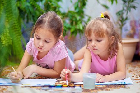 两个女孩在家里或幼儿园的地板上用颜料作画。