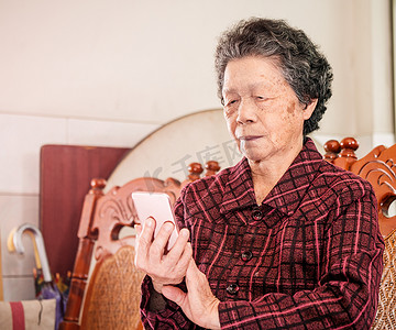 亚洲老年妇女坐在现代智能手机上浏览某些东西，与家里的其他人建立联系，生活技术，特写