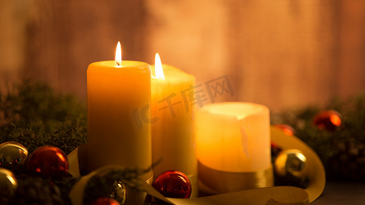 圣诞节概念的温暖：三支蜡烛的特写，在深色木桌上点燃，配有松枝、天然松果、金色和红色明亮的小玩意，配有金色缎带