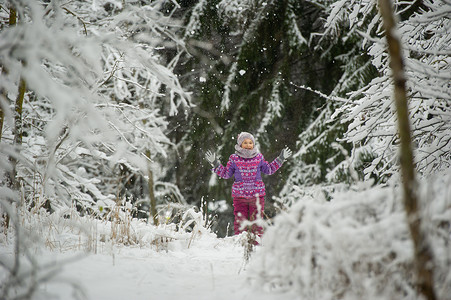 紫色衣服摄影照片_一个冬天穿着紫色衣服的小女孩穿过白雪覆盖的森林