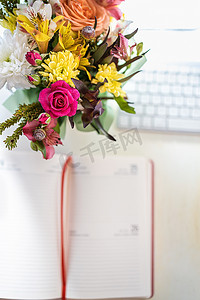 灵感本摄影照片_键盘附近的桌面上有一束时尚的鲜花，上面有新鲜的春天的花朵和手写的纸质笔记本 - 一本日记。