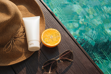 泳池边的橙汁、草帽、防晒霜和太阳镜