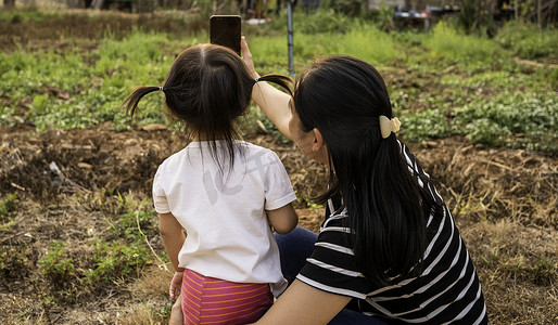 亚洲小女孩在日落背景下在花园里与母亲合影的后视图。