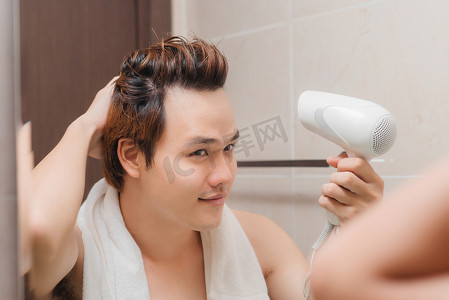 帅哥洗完澡后用吹风机吹干头发，微笑着看着镜子里的自己