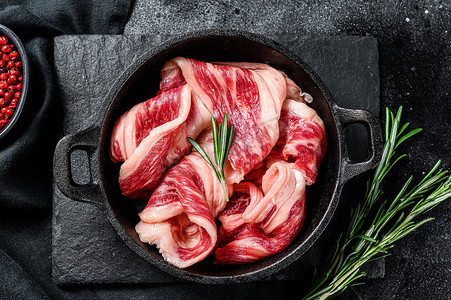 肉条摄影照片_生培根，平底锅里的大理石纹肉条。