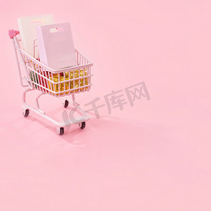 浅粉色背景摄影照片_年度销售购物季概念 — 迷你红色商店推车，里面装满纸袋礼物，浅粉色背景，空白复制空间，特写