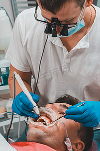 牙医在诊所，牙垢去除程序，双筒望远镜的牙医去除患者口腔中的牙垢。
