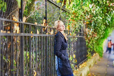 巴黎街头摄影照片_阳光明媚的秋日或春日，巴黎街头的年轻女子