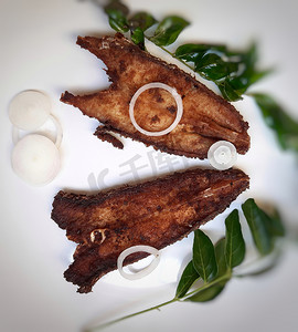 印度餐厅风格的辣鱼苗放在白盘中，并用咖喱叶和洋葱镀得很漂亮