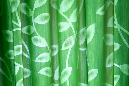 绿色窗帘摄影照片_带有叶子图案的绿色窗帘从房间外面闪耀着有趣的阴影。