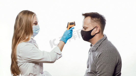使用戴着医用口罩和蓝色一次性手套的非接触式温度计护士检查患者体温测试。