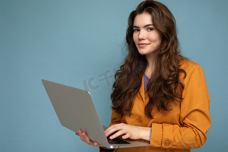 美丽的年轻女子拿着电脑笔记本电脑看着相机的照片在彩色背景中被隔离