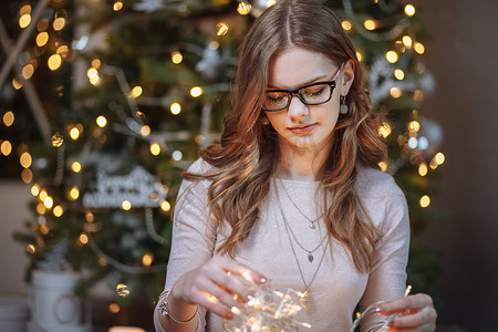 一年一摄影照片_圣诞节时，在一棵新年树的背景上，一个戴着花环、戴着眼镜的微笑女孩的画像