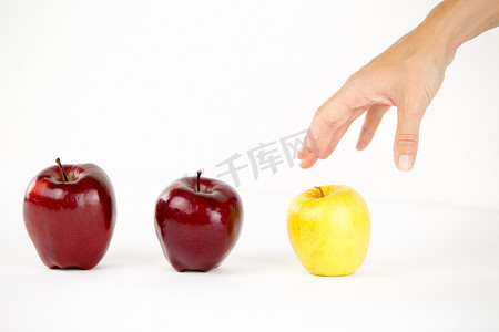 多样性的概念：一个女人的手即将抓住其他红苹果中唯一的黄苹果