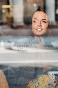 坐在窗边的咖啡馆里，一个留着长发的年轻欧洲女孩的画像，一个穿着长发夹克的高个子女孩，在咖啡馆的窗户反射下