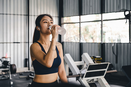 喝水摄影照片_亚洲年轻女性在健身房锻炼后喝水、健康和运动概念。