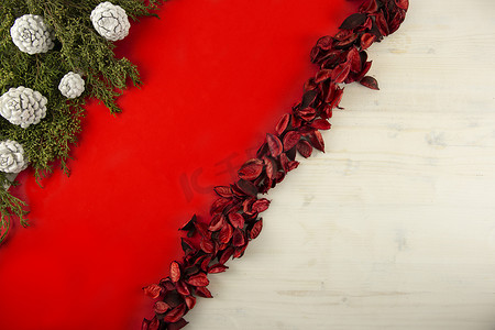红色大气丝带背景摄影照片_平铺的红色圣诞复制空间，在浅色木质背景、松枝、白松果和红色花瓣上有一条对角线红色条纹
