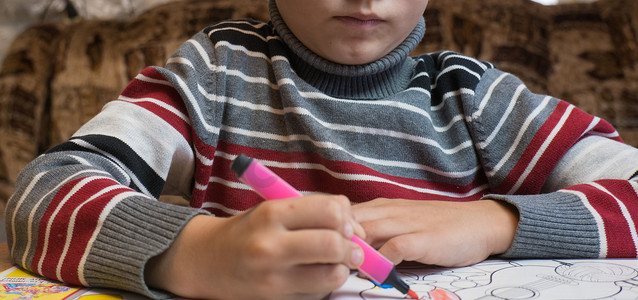 一个小男孩在家里的木桌上用蜡笔和毡尖笔涂色