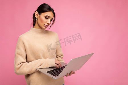 商业活动照片摄影照片_侧面照片：迷人、悲伤的年轻女士拿着笔记本电脑，隔离在墙壁背景上，低头看着上网本