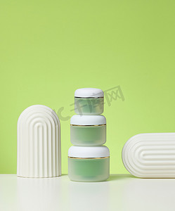 白色桌子上的化妆品的绿色罐子。