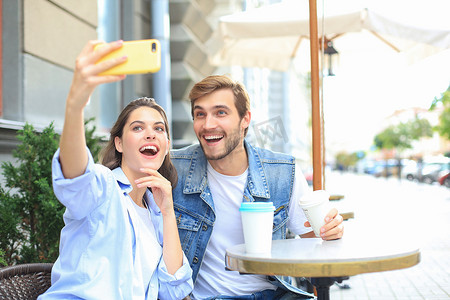 美丽的年轻恩爱夫妻在咖啡馆里相互依偎，而女人则用智能手机自拍。