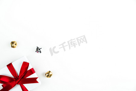 美丽的节日或圣诞节背景图像，一个小红丝带包裹着白色盒子礼物或礼物在左下角，白色背景上有银色和金色的铃铛和复制空间。