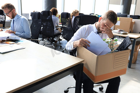 悲伤的被解雇工人正带着他的办公用品离开办公室