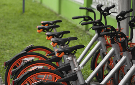街道交通橙色混合租赁自行车以电子支付方式在城市中行驶，在租赁网络停车场排成一排，等待骑自行车的人骑自行车旅行。