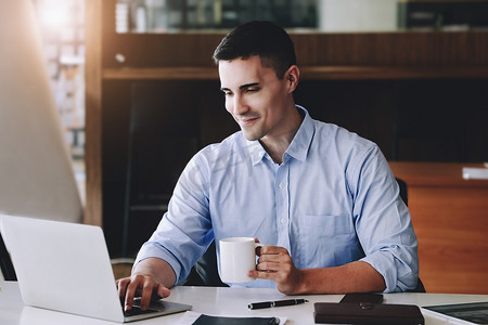 在使用电脑、iPad 和营销分析文件之前，男性营销经理一边工作一边喝咖啡以减少睡意。