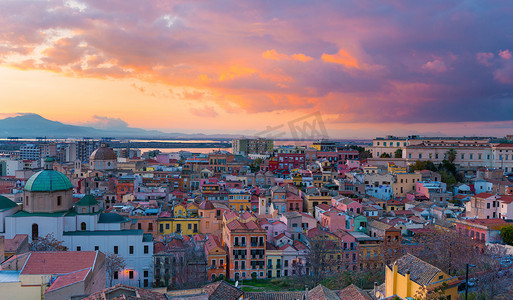 卡利亚里的日落，旧城中心的全景，有传统的彩色房屋、山脉和天空中美丽的黄粉色云彩，意大利撒丁岛
