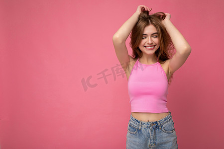 年轻的微笑美丽的深色金发女人带着真诚的情感被隔离在背景墙上，复制空间穿着时尚的粉红色上衣。