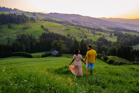 住宅风景摄影照片_瑞士乡村，Ebnat Kappel，瑞士圣加仑，一对男人和一个女人在瑞士草地上的小屋外看日落