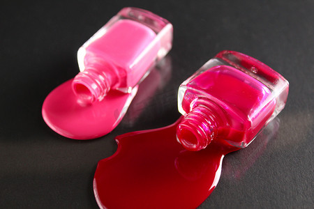 美容背景两瓶指甲油瓶红色或勃艮第粉色溢出物倒在黑色背景的桌子上，从顶部的侧面特写视图，带有复制空间
