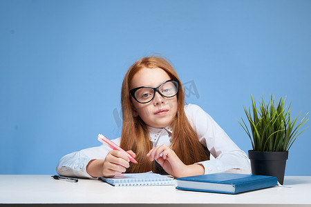 戴眼镜的红发女孩在学校教育桌上做作业