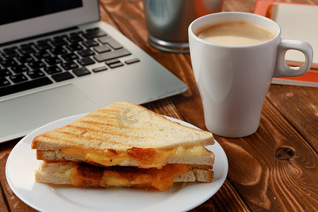 在木办公桌上的三角三明治与膝上型计算机和咖啡杯
