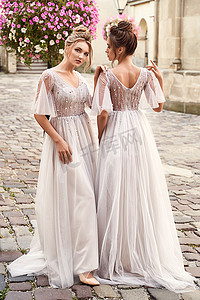 婚礼当天，两位美丽的伴娘女士身穿华丽优雅时尚的浅灰色银色拖地露背礼服，在古老美丽的欧洲城市。