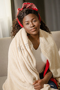 扎带摄影照片_头戴领带的非洲裔美国妇女坐在毛绒毯子里。