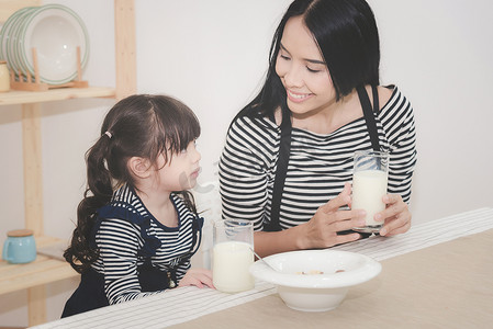 早上喝牛奶摄影照片_亚洲妈妈的幸福家庭早上和她可爱的女儿一起喝牛奶。