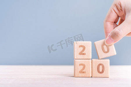 摘要 2020 年和 2019 年新年倒计时设计理念 — 女性在木桌和蓝色背景上拿着木块立方体，特写，复制空间。