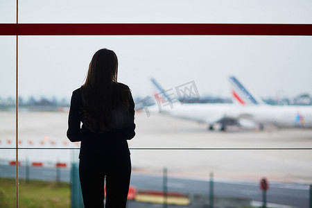 国际机场提着手提行李的女人，透过窗户看飞机