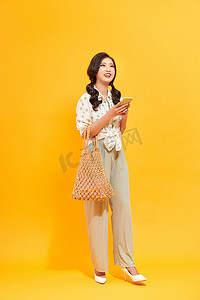 年轻漂亮的亚洲女士拿着手机，看起来兴奋而快乐，手里拿着手提包