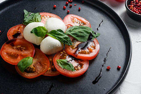 Caprese 新鲜意大利沙拉配西红柿、马苏里拉奶酪、绿色罗勒，白色背景的深色石板上特写选择性焦点