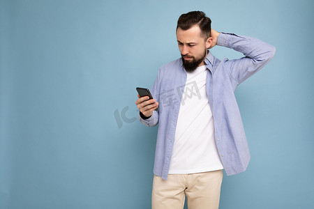 侧面照片拍摄的英俊英俊的年轻人穿着休闲时尚的服装，在背景中与世隔绝，手拿空地，使用手机短信看着智能手机显示屏并思考