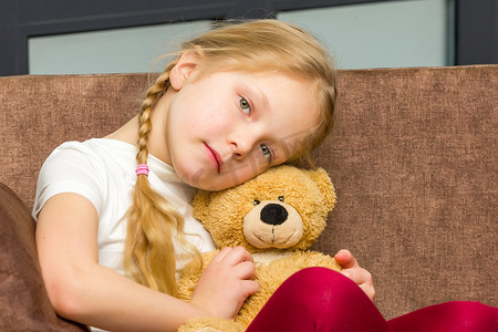 沙发上抱着泰迪熊的小女孩。