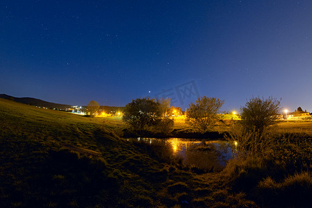 蓝色的星空倒映在小池塘里，与橙色的路灯形成鲜明对比。