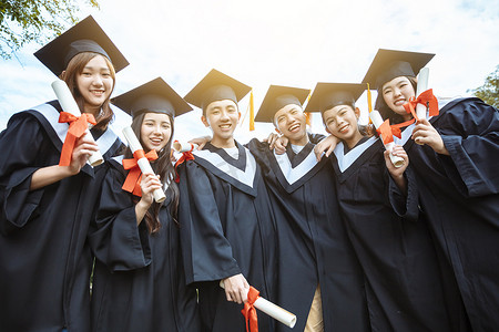 男人毕业摄影照片_穿着毕业礼服的快乐学生在大学校园里持有文凭