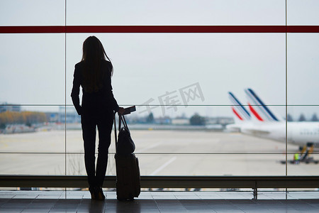国际机场提着手提行李的女人，透过窗户看飞机