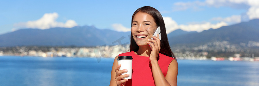 宽横幅摄影照片_快乐的女人一边打电话一边在夏日阳光下的户外喝咖啡，横幅作物用于广告复制空间，背景是温哥华的风景。